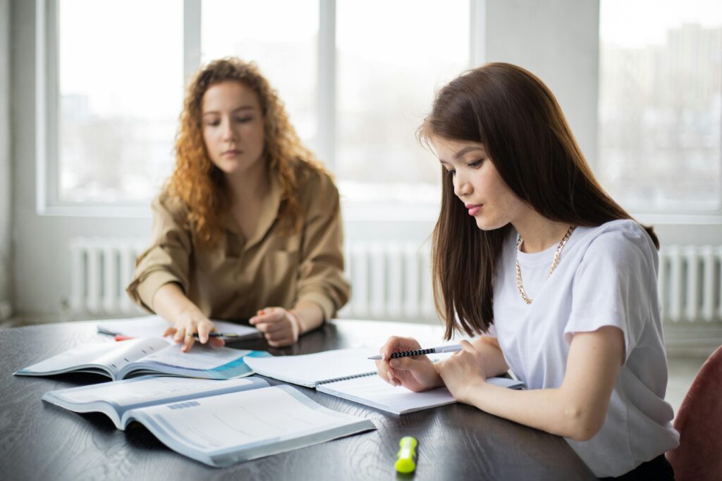 Two young women concentrating on study materials in a well-lit classroom environment.